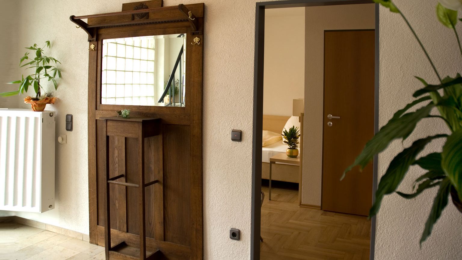 Eingangsbereich und Flur des Gaestehaus Birkenhof Alzey im Flur steht eine Holzkommode mit Spiegel dahinter geoeffnete Zimmertuere mit Blick ins Einzelzimmer